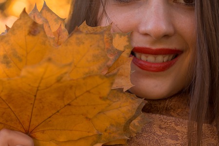 girl with red lipstick on lips keeps autumn leaf near the faceの写真素材