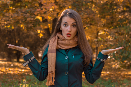 young woman in scarf stands in the park looks straight and hand holds on the sidesの写真素材