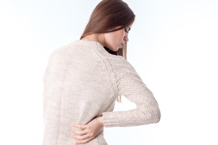 a girl in a sweater stands with his back to the camera keeps a hand on the side of feeling pain is isolated on a white.の写真素材
