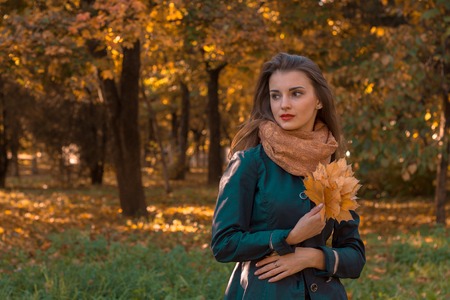 girl in a black cloak stands in the Park keeps leaves and looks awayの写真素材