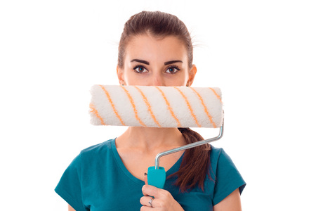portrait of young beautiful brunette building woman in uniform with paint roller in hands makes...