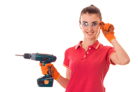 young happy woman with dark hair in uniforl makes renovations with drill in her hands isolated on whiteの写真素材