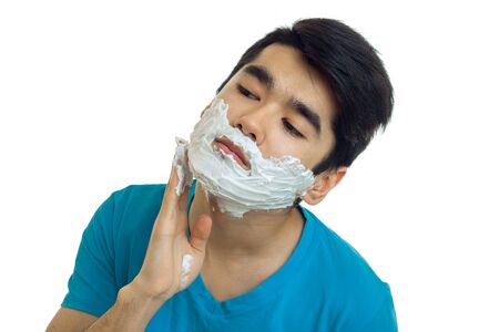 handsome young guy with black hair head tilted to the side and rubs the foam on his face isolated on...