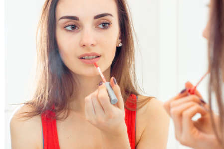 very beautiful young girl colors lip gloss in the bathroom front of the mirror close-up