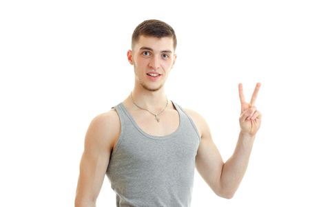 handsome gay guy looks into the camera and hand gesture with raised up two fingers is isolated on a white backgroundの写真素材