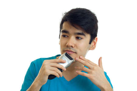 handsome young guy in a t-shirt looking sideways and shaves a beard trimmer close-up isolated on white backgroundの写真素材