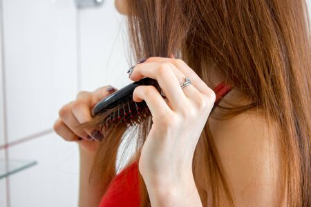 close up of woman in red t-shirt combs her hair in bathroom
