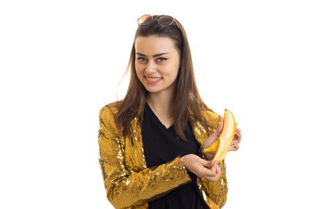 Cheerful stylish girl in golden jacket with banana smiling on camera isolated on white backgroundの写真素材