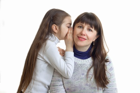 close-up portrait of a little girl who whispers something in his ear to her mum is isolated on a white backgroundの写真素材