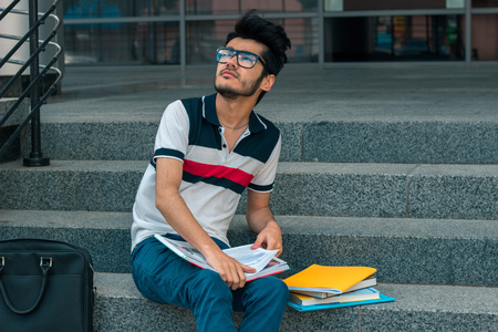 a young thoughtful student in a t-shirt sits with books on the stairs and looks aheadの写真素材