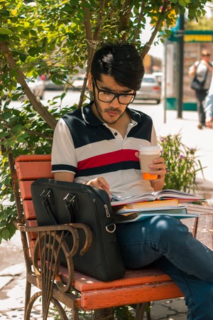 vertical portrait of beautiful glamorous guy in glasses with a book and a cup of coffee in handの写真素材