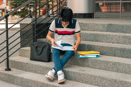 young fashion guy reads books sitting on the streetの写真素材