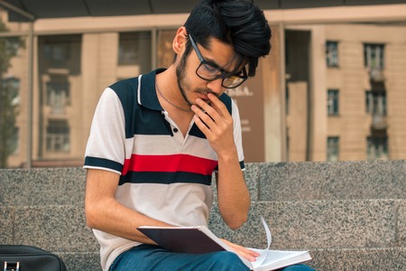 a close-up portrait of charming young man in glasses and a book in his handの写真素材