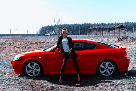 gorgeous young slim woman in sunglasses stand witha red sports car in the fieldの写真素材