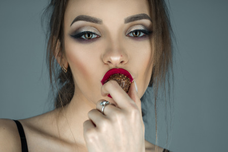 sexual girl with red lips eats chocolate candy and looking at the camera in studioの写真素材