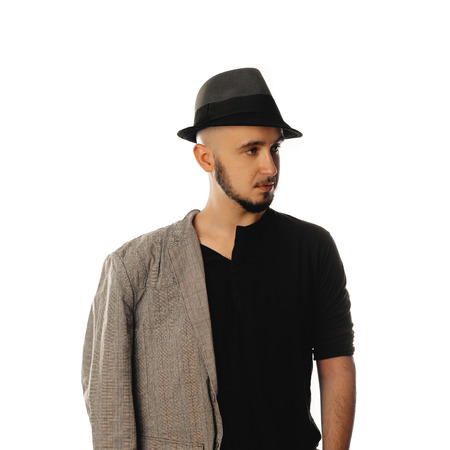 serious young unshaved man in hat and jacket looking away isolated on white background in studioの写真素材