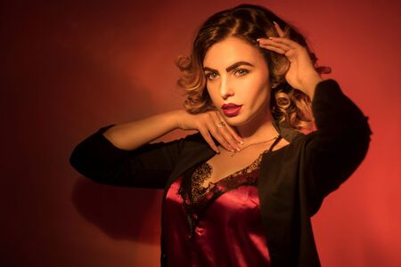 Adorable young lady with curly hairstyle and red lips posing in red studioの写真素材