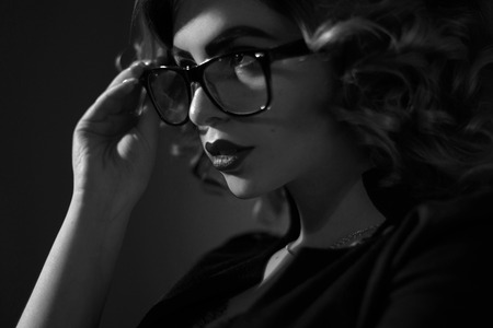 black and white photo of Sexy young secretary in glasses and curly hairstyle in studioの写真素材