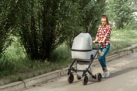 Stylish young mom walks with stroller in the park