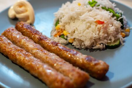 baked sausages and rice with vegetables on blue plateの写真素材