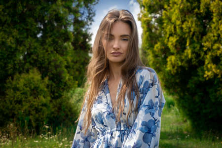 Beautiful young lady in dress with flower print looking at the camera at green park