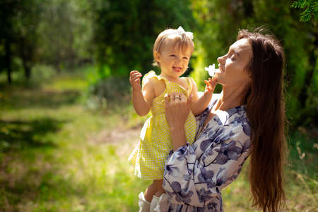 happy stylish young mother plays with her little daughter at the green gardenの写真素材