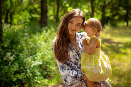 happy stylish young mother plays with her little daughter at the green gardenの写真素材