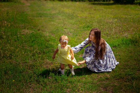 happy stylish young mother plays with her little daughter at the green garden