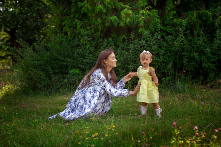 portrait of young happy stylish young mother plays with her little daughter at the green gardenの写真素材