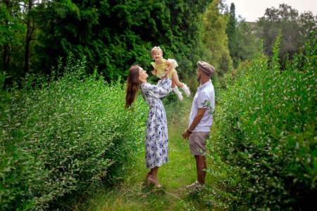 Cheerful young parents playing with their little baby girl at the green garden. Happy family having fun at the parkの写真素材