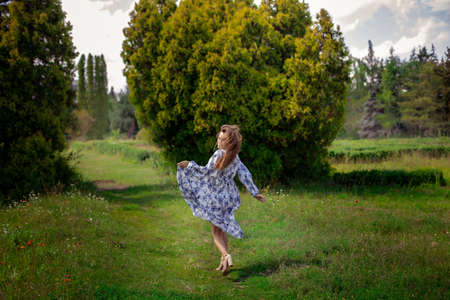 Glamour brunette girl on high heels runs in long dress with flowers print at the parkの写真素材