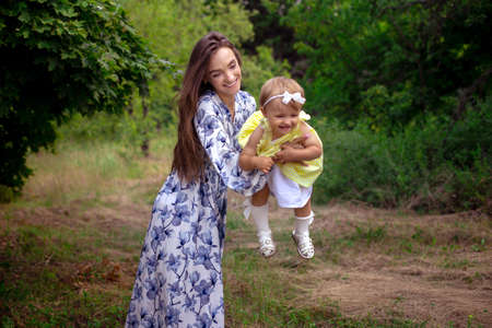 horizontal portrait of Cheerful mother plays with her little baby girl and smiles at the parkの写真素材