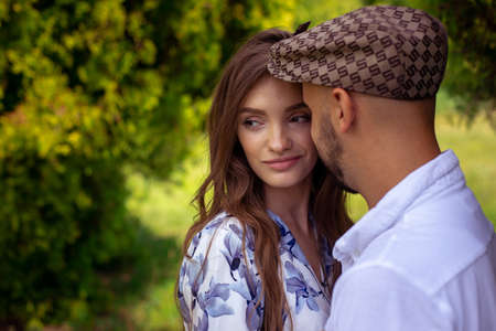 stylish young man hugs his pretty girl when she smiles and looking away at the green gardenの写真素材