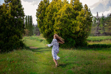 Cheerful brunette woman on high heels walks in long dress with flowers print at the parkの写真素材