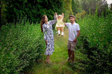 Happy young parents playing with their little baby girl at the green garden. Cheerful family having fun at the parkの写真素材