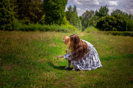 Mom points finger her little daughter to the green grass at the garden in warm summer dayの写真素材