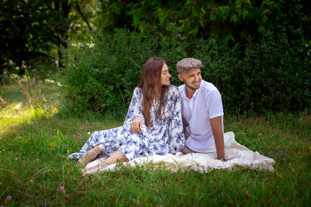 beautiful caucasian couple in love at the picnic sits on the blanket and looks away at the grren meadowの写真素材