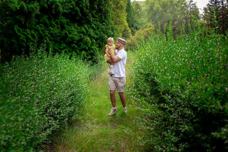 stylish young caucasian dad walks carrying little daughter at the gardenの写真素材