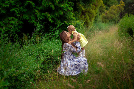 happy stylish mother carrying her little daughter at the green gardenの写真素材