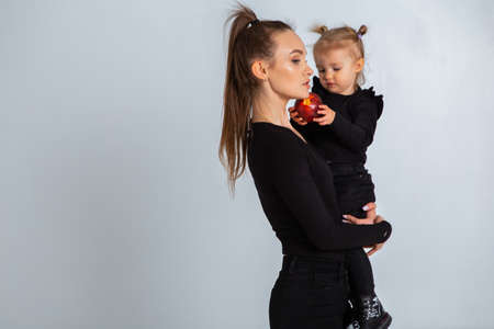 Sexy young mother in black clothes hold her little daughter in hands in studioの写真素材