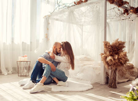 Beautiful couple in love hugs and kisses in white room at homeの写真素材