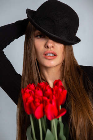 portrait of a beautiful girl in a hat with tulips in hands in studioの写真素材