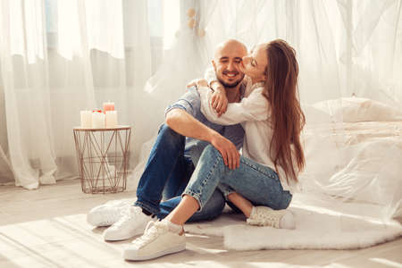 Beautiful couple in love hugs and kisses in white room at homeの写真素材