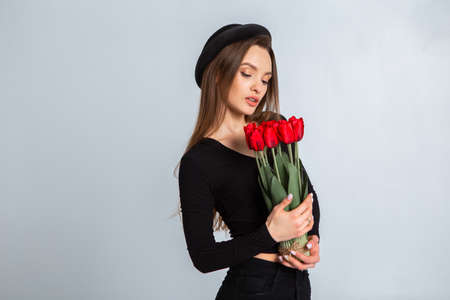 portrait of a beautiful girl in a hat with tulips in hands in studioの写真素材