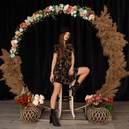 Beautiful woman posing at circle of deadwood in dress with flower print in studioの写真素材