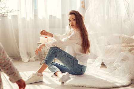 Charming caucasian woman sits in front of bed at light room at homeの写真素材