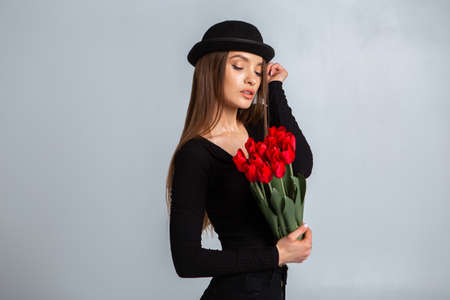 portrait of a beautiful girl in a hat with tulips in hands in studioの写真素材