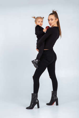 Sexy young mother in black clothes hold her little daughter in hands in studioの写真素材