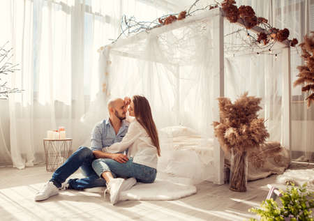 Beautiful couple in love hugs and kisses in white room at homeの写真素材