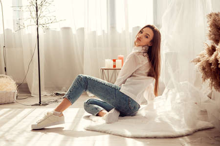 Charming caucasian woman sits in front of bed at light room at homeの写真素材